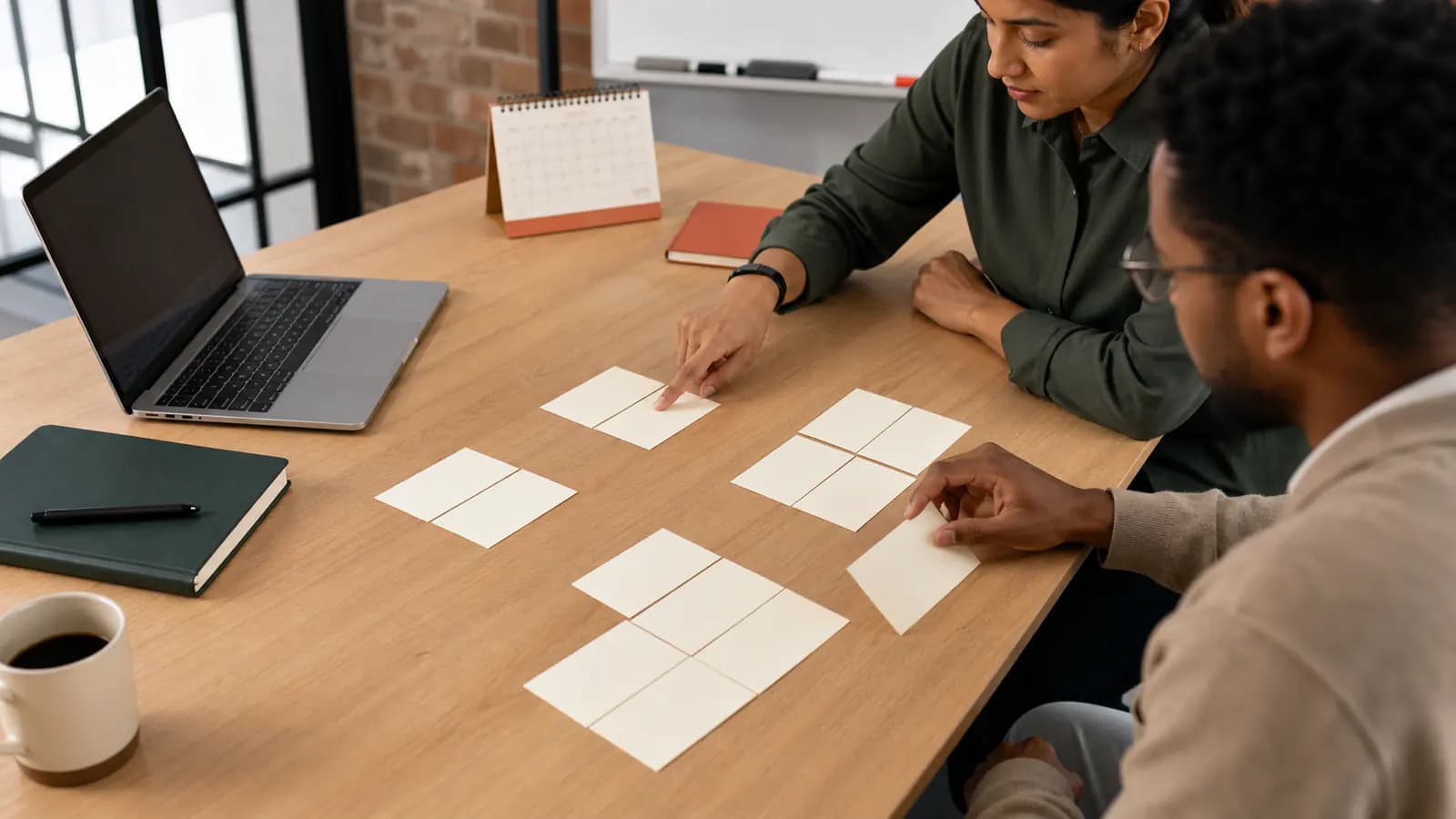 Two colleagues arranging blank evidence cards into groups beside a laptop and calendar